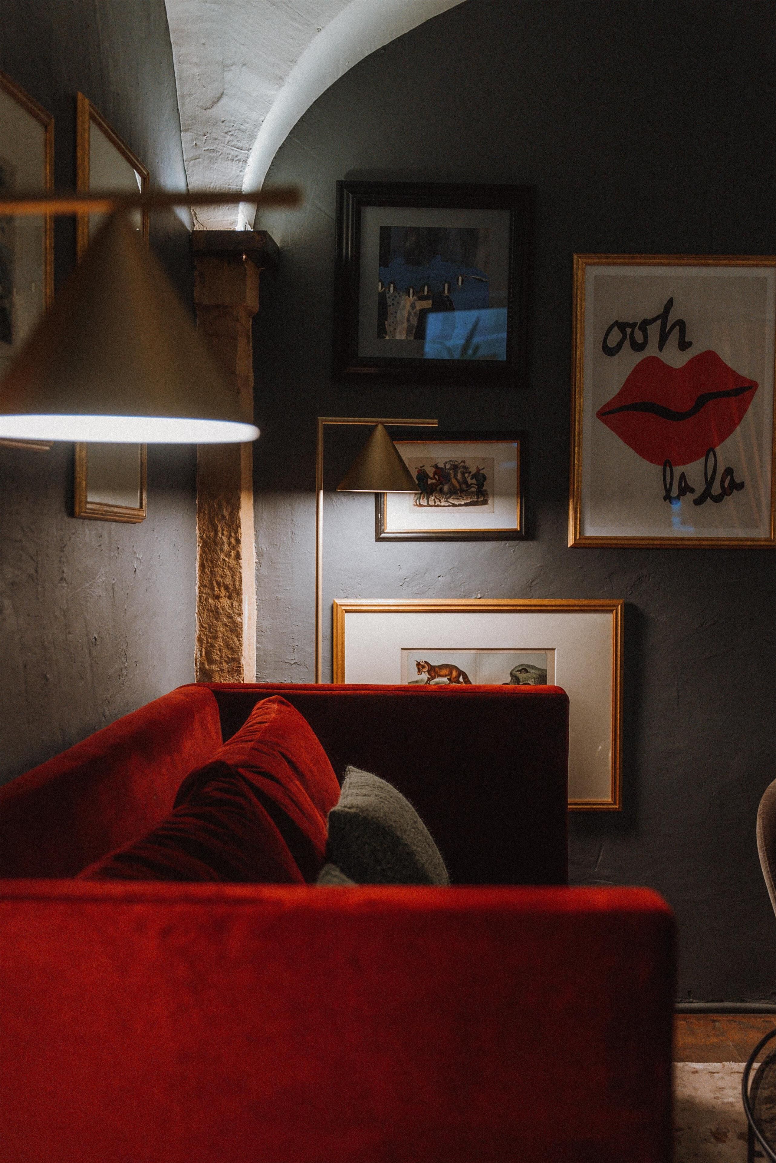 A cozy room with a red sofa, a lamp, and framed pictures on the wall.