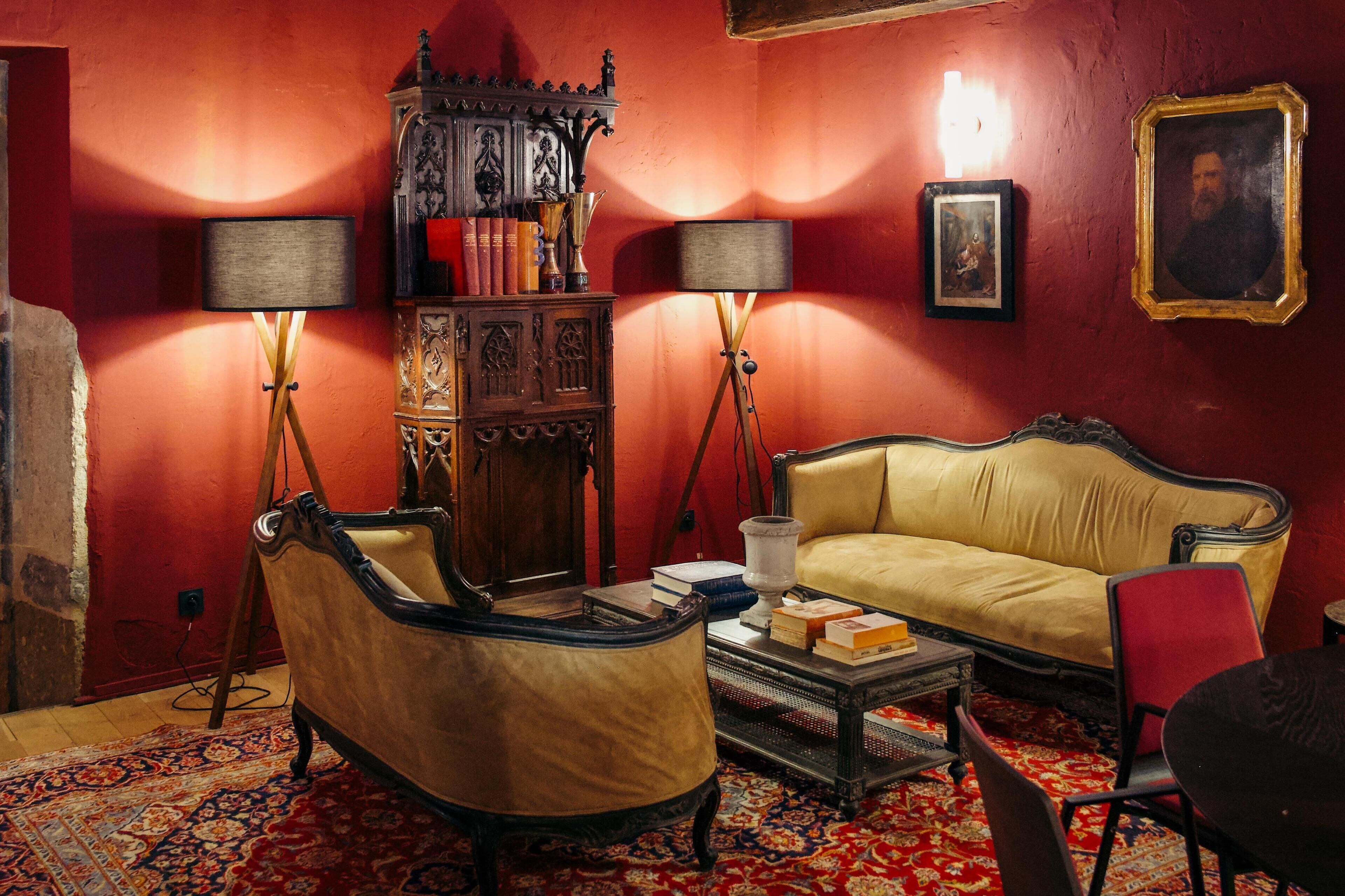 Quarto com parede vermelha, sofá amarelo, armário de madeira, duas luminárias de chão e tapete estampado.