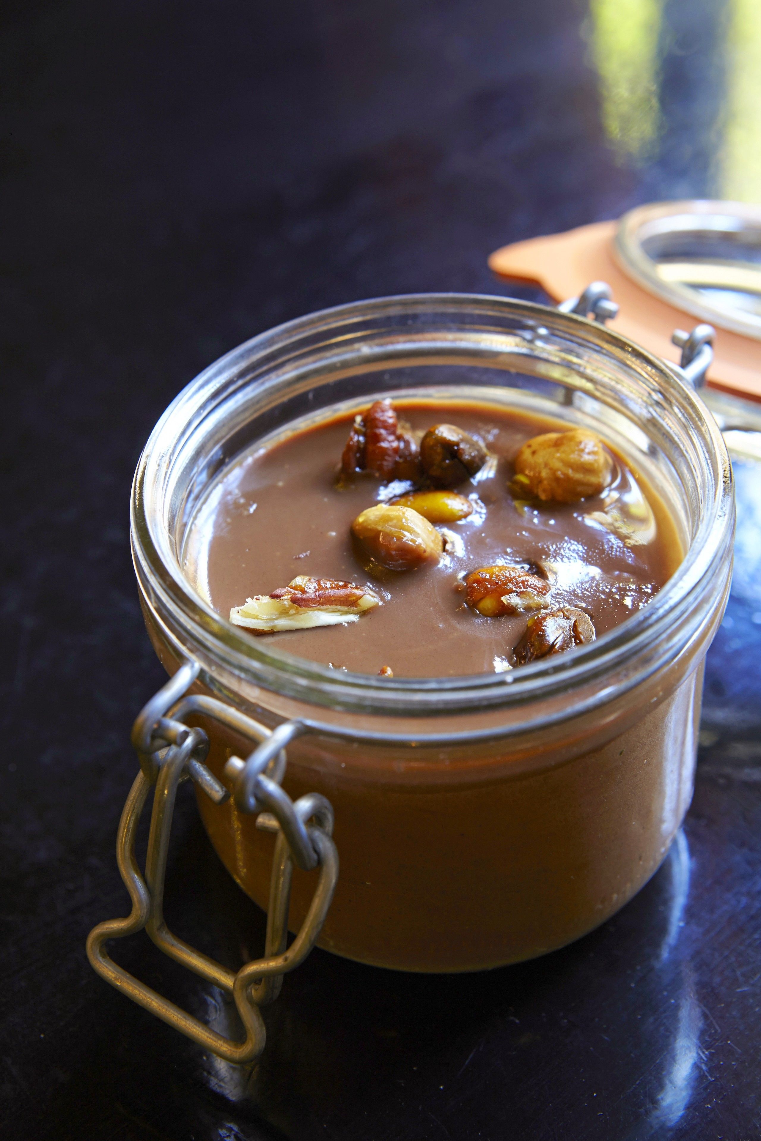 Un tarro de crema de chocolate con nueces sobre una superficie oscura.