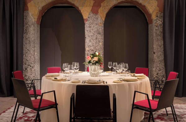 A formal dining room with a round table set for a meal, red chairs, and a decorative vase centerpiece.