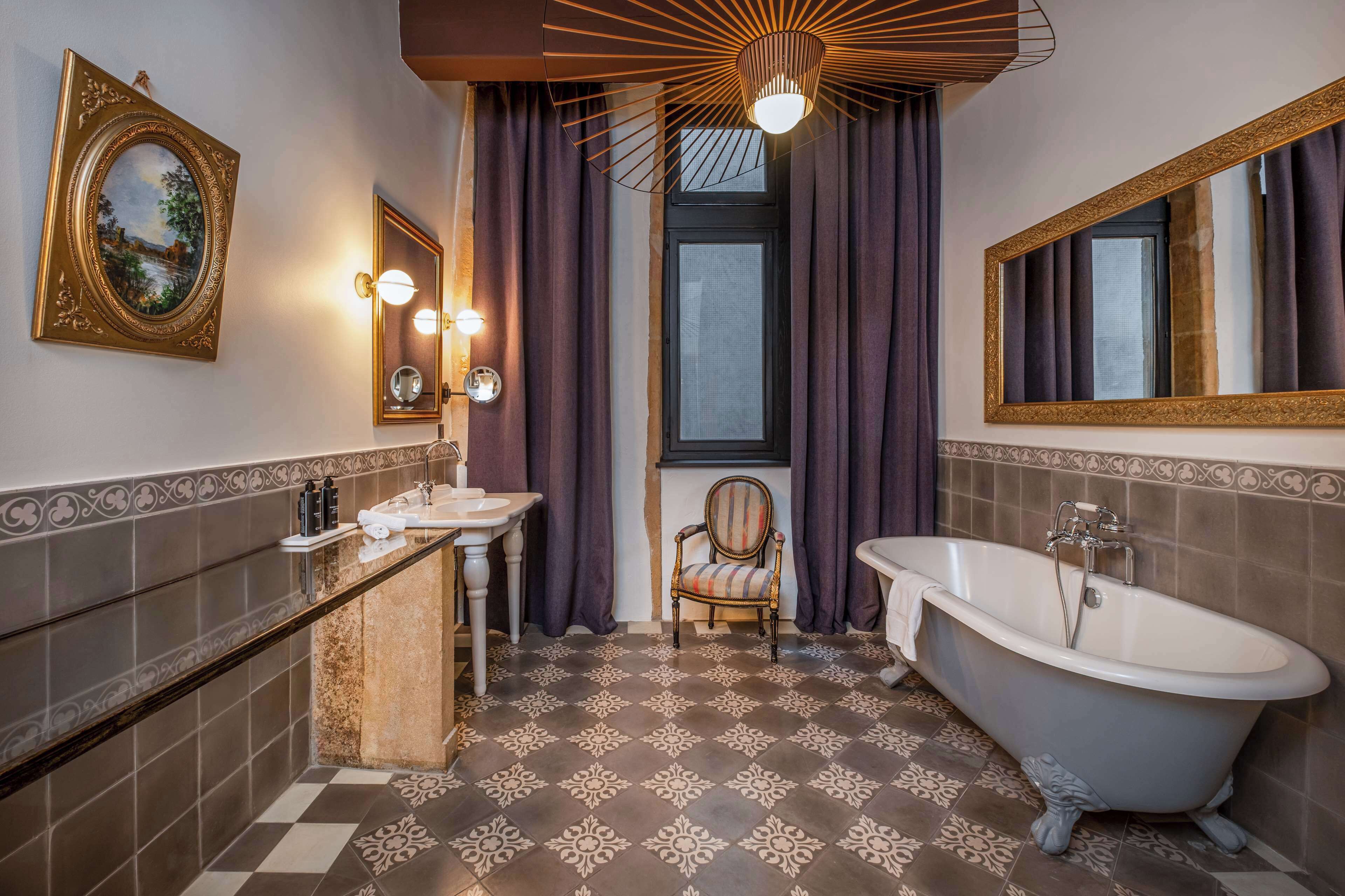 A bathroom with a bathtub, a vanity with a mirror, a chair, and a window with curtains.