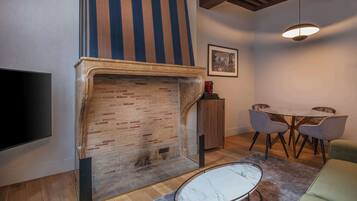 Un salon doté d’une cheminée en briques, d’un téléviseur à écran plat, d’un coin repas avec une table et des chaises, et d’un luminaire suspendu.