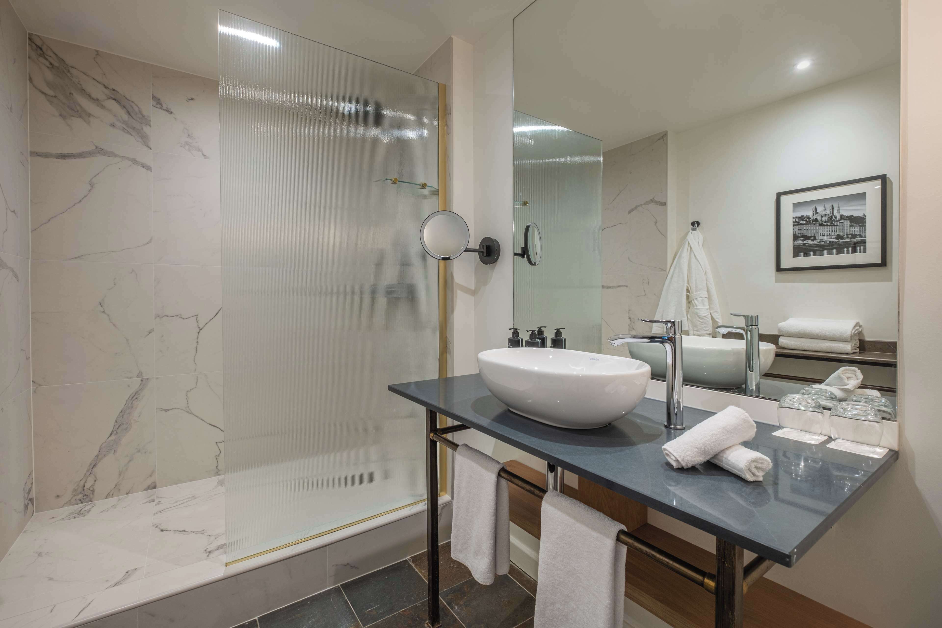 A modern bathroom with a large mirror, a white sink, and a glass shower enclosure.