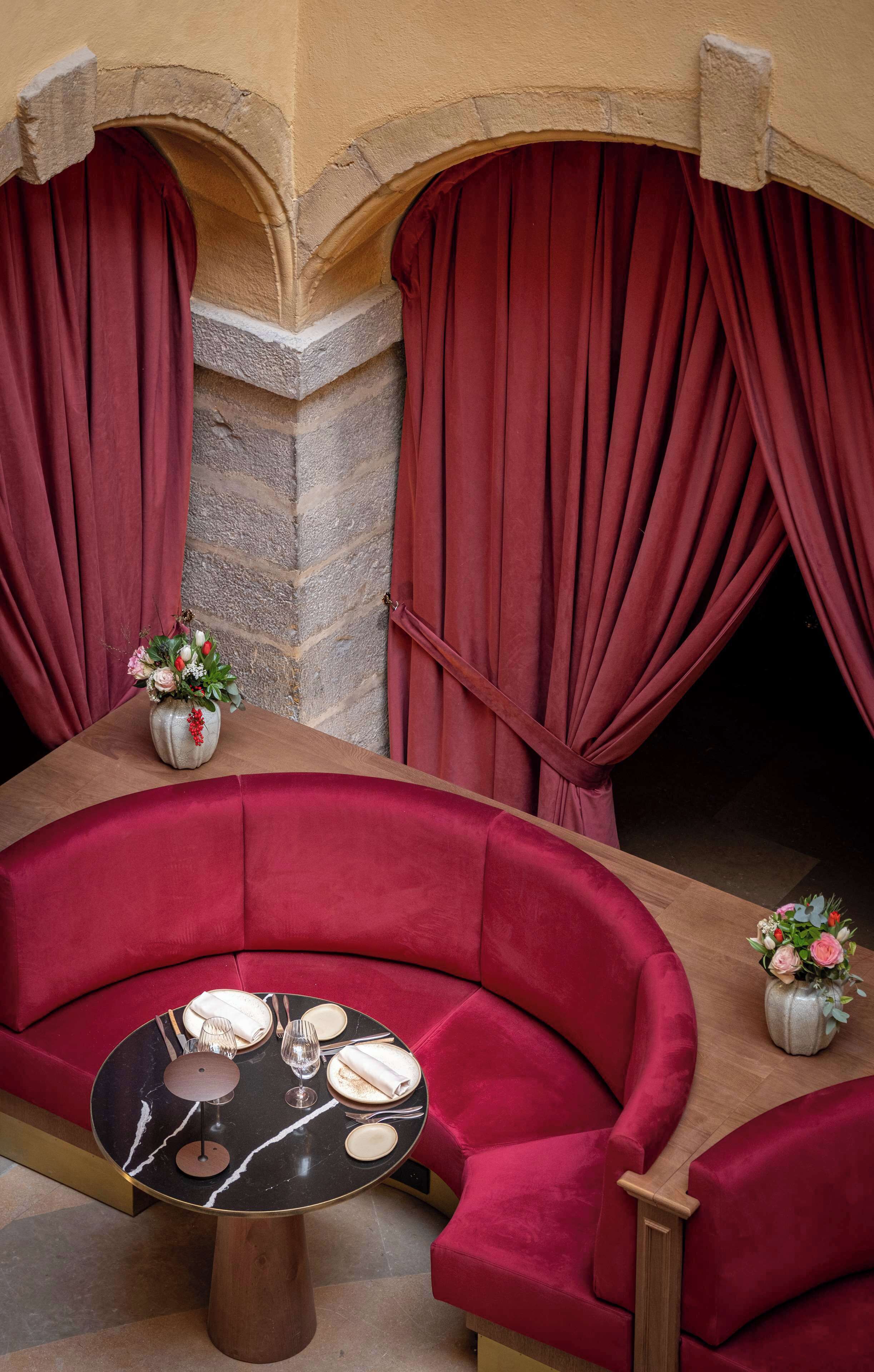 A red upholstered sofa, a round table with a black marble top, and a vase with flowers.