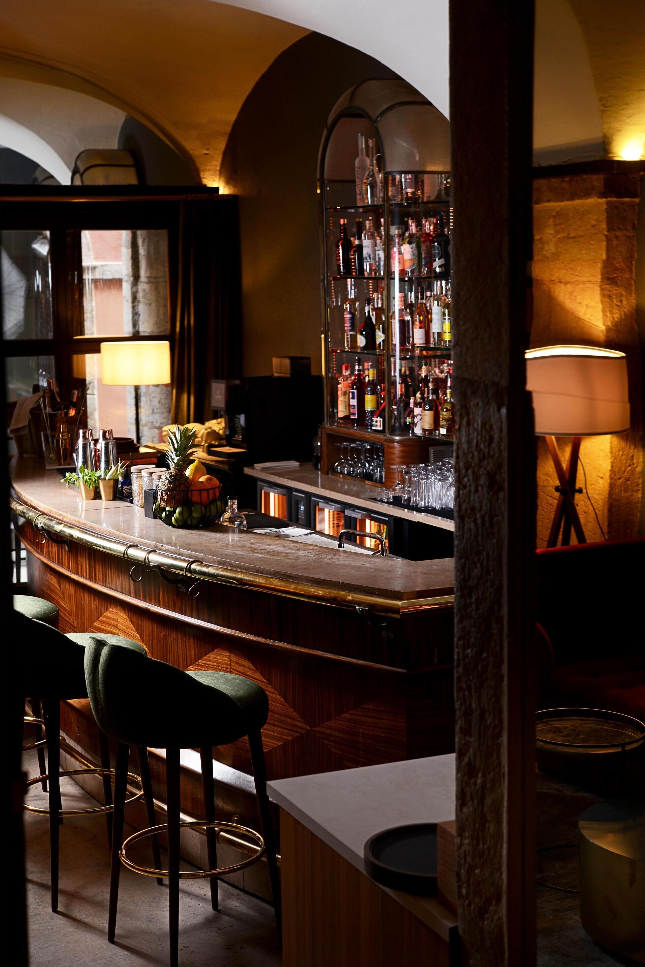 A bar area with a wooden counter, bar stools, a well-stocked liquor shelf, and a lamp.
