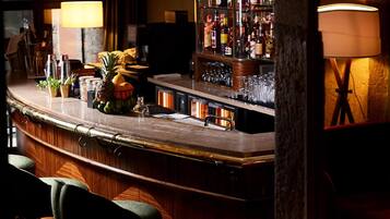 A bar area with a wooden counter, bar stools, a well-stocked liquor shelf, and a lamp.