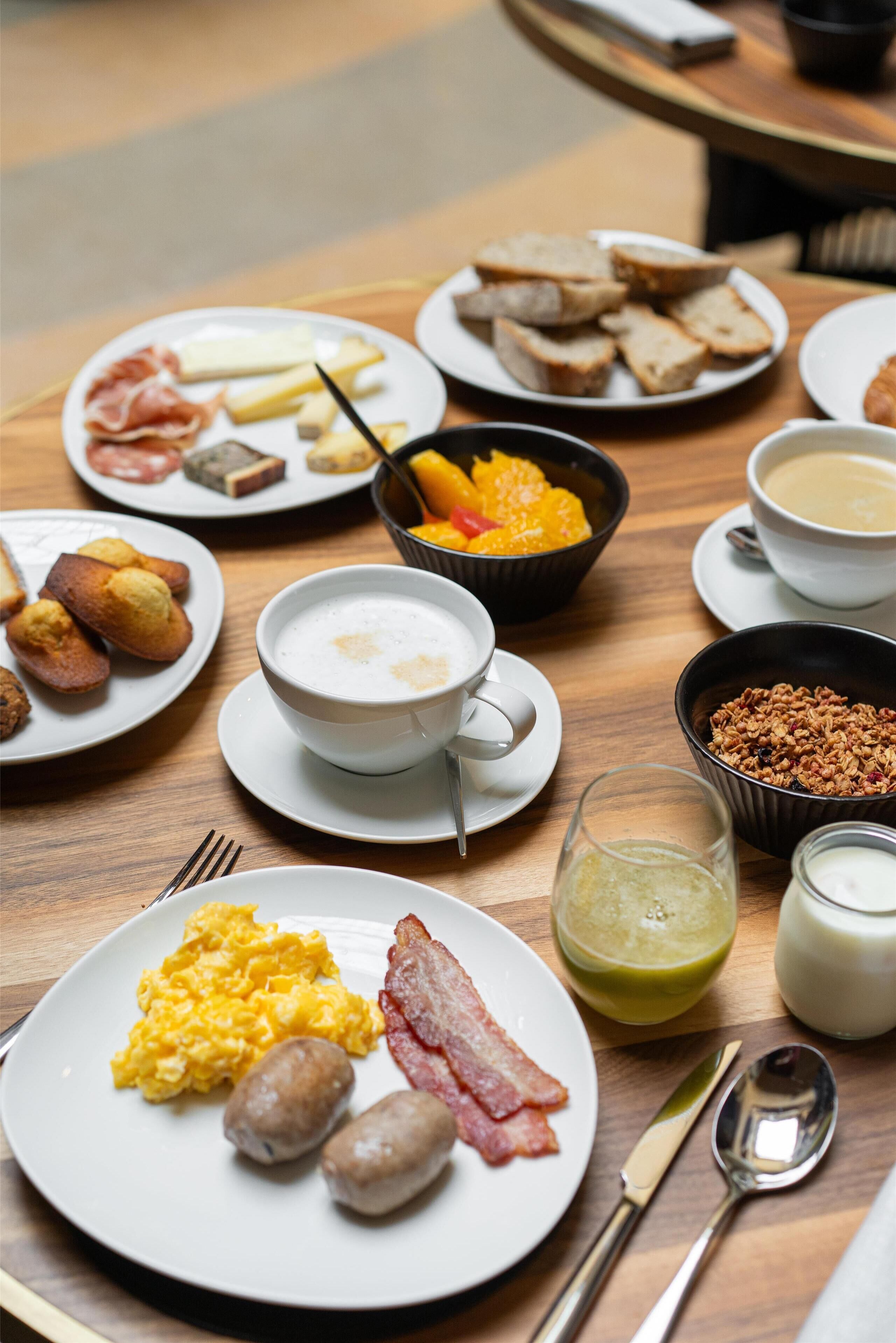 A breakfast table with plates of eggs, bacon, sausages, toast, and fruit.