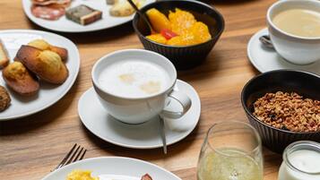 A breakfast table with plates of eggs, bacon, sausages, toast, and fruit.