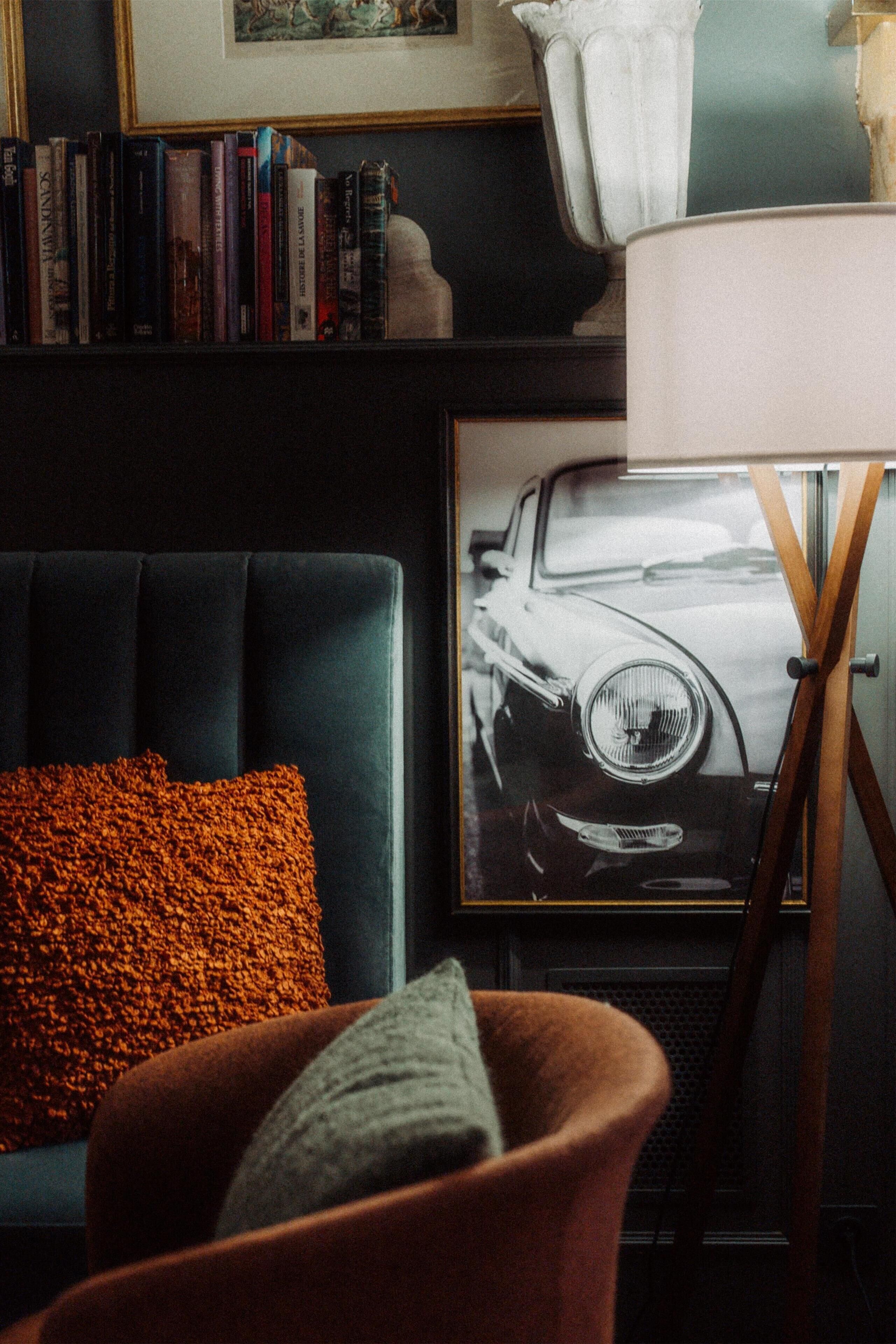 Un soggiorno con un divano scuro, un quadro di un'auto e una libreria.