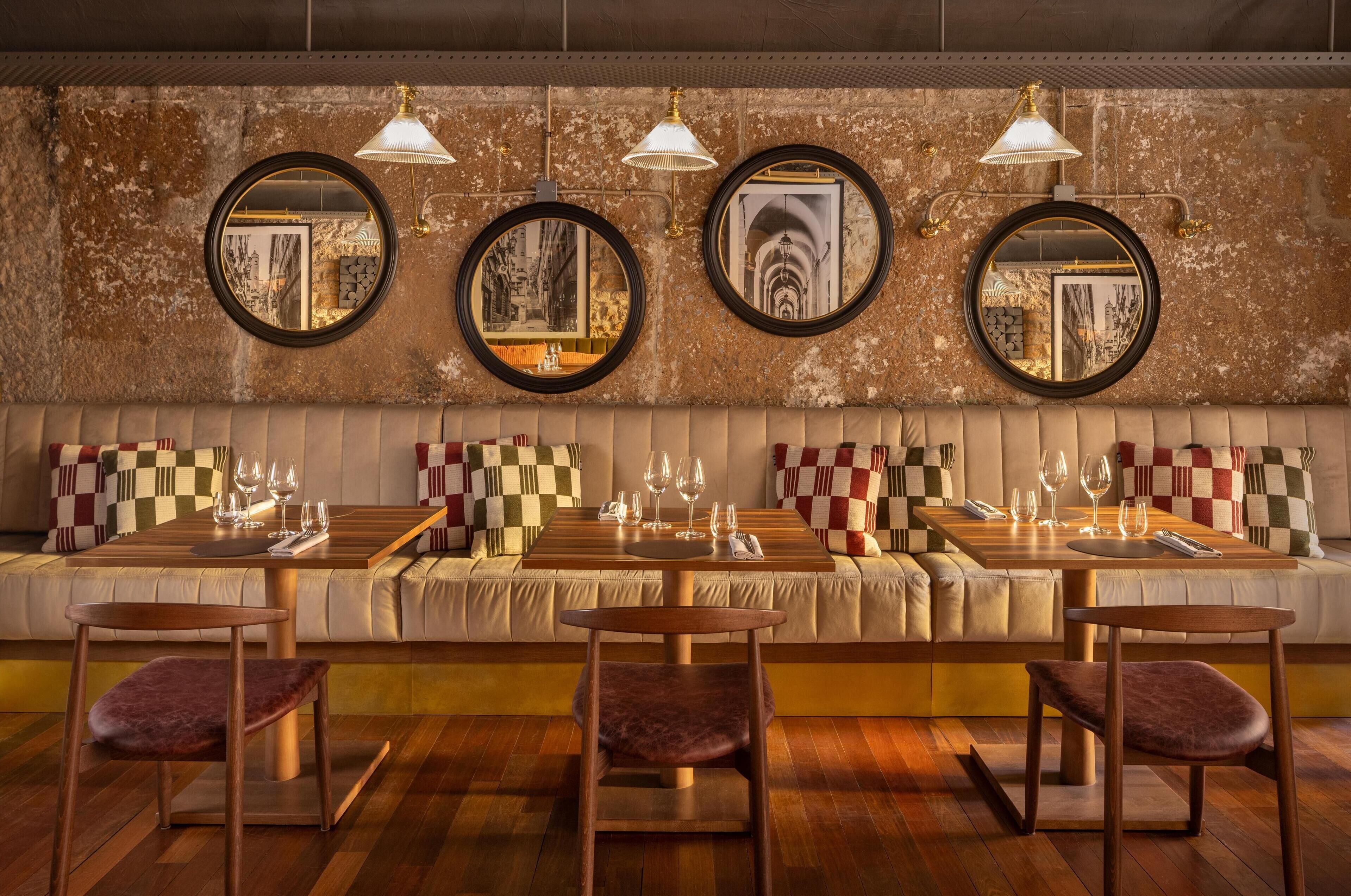 Ein Restaurant mit einer langen Sitzbank, mehreren runden Spiegeln an der Wand und Holztischen mit Stühlen.