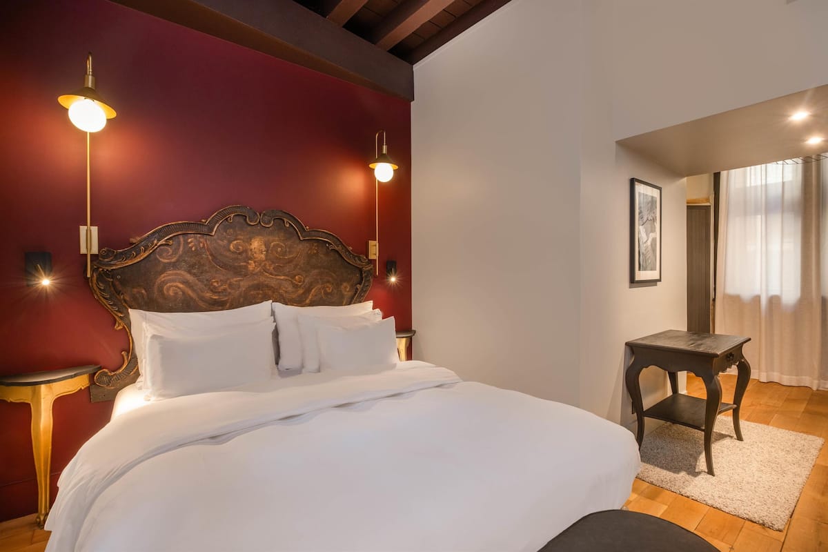 A neatly made bed with a wooden headboard, two bedside lamps, and a small wooden table with a rug.