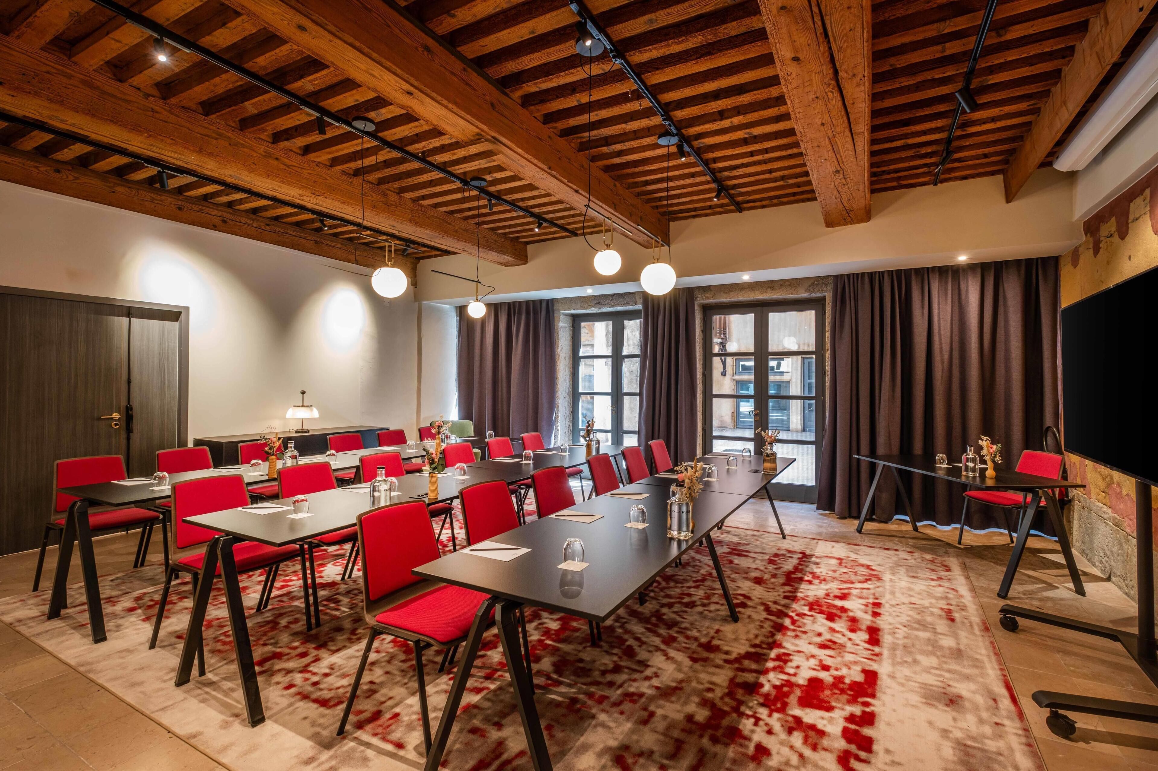 A conference room with a long table, red chairs, and a wooden ceiling.
