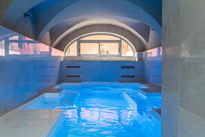 Una piscina interior con vistas al exterior a través de un amplio ventanal de arco.
