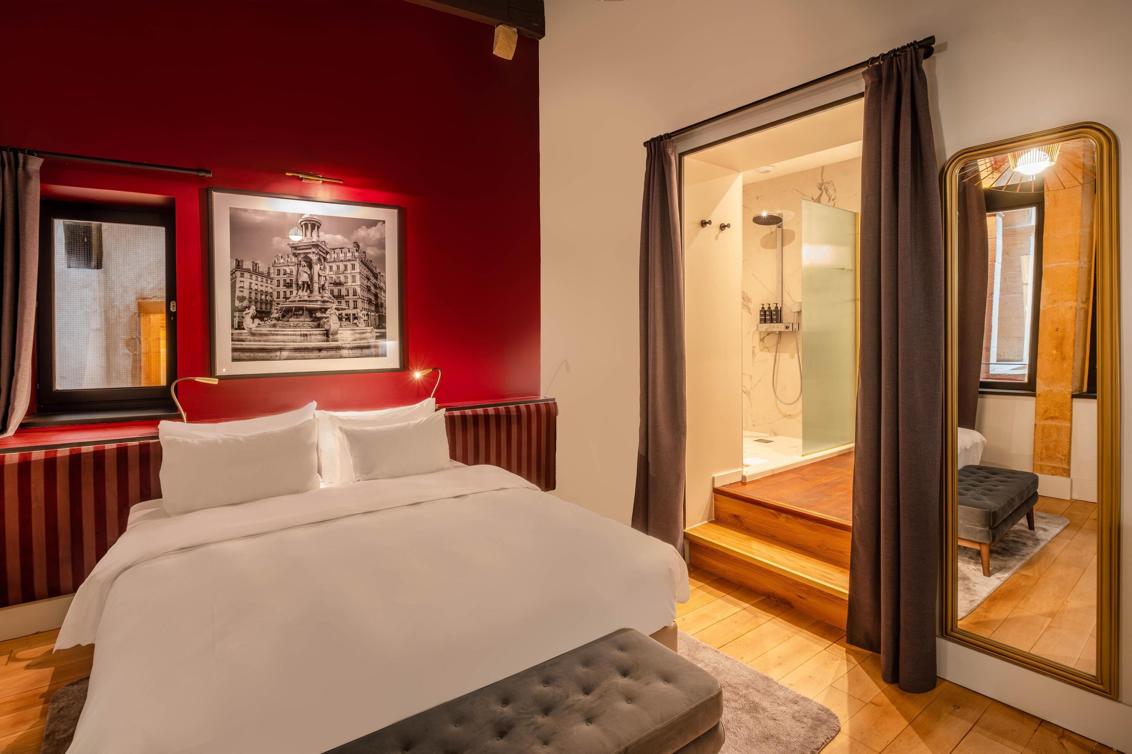 A hotel room with a bed, a large mirror, a shower area, and a framed picture on the wall.