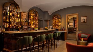 A bar area with a wooden bar, multiple stools, and shelves stocked with bottles.