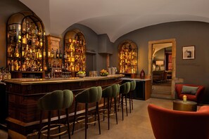 A bar area with a wooden bar, multiple stools, and shelves stocked with bottles.