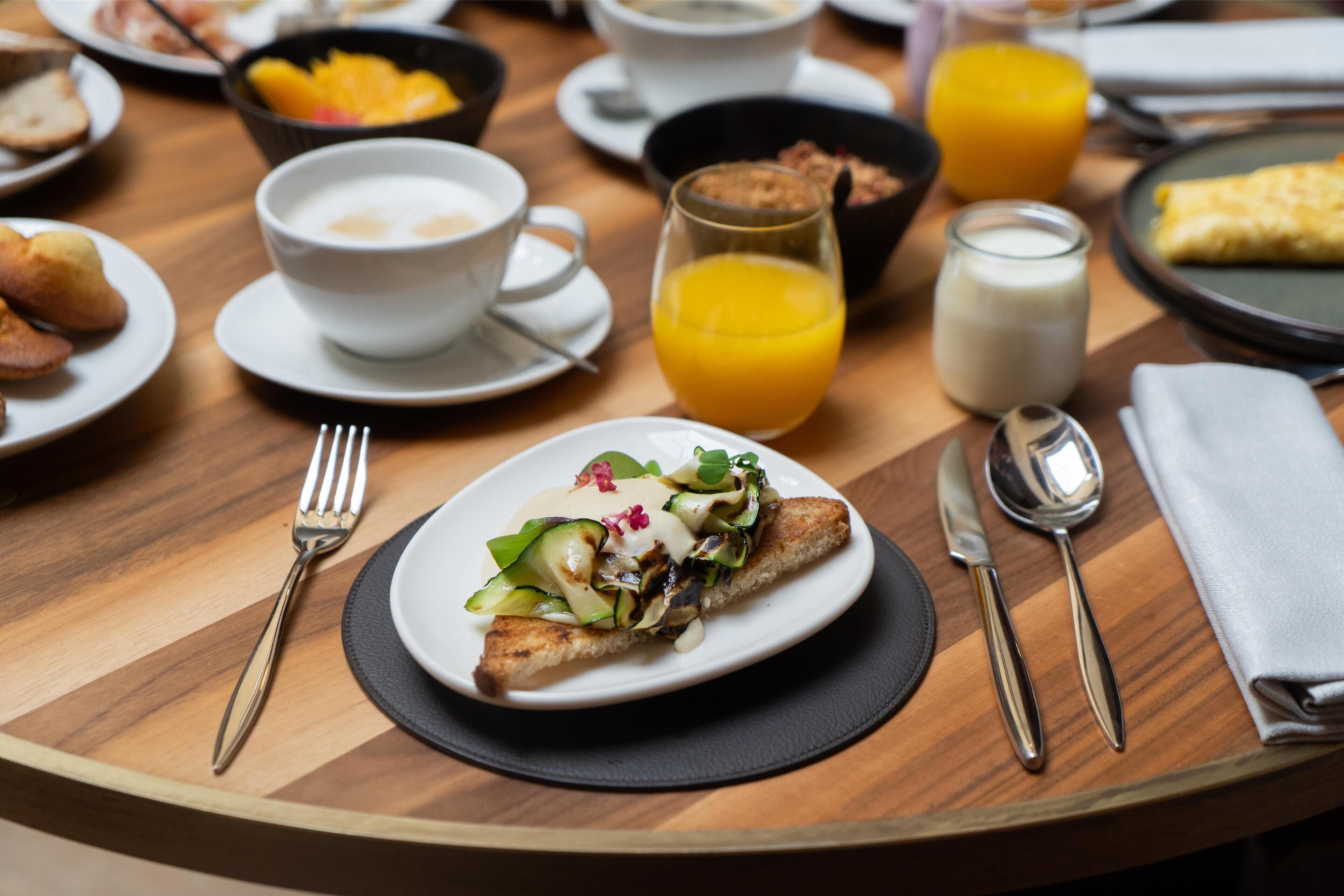 Un desayuno con un plato de comida, un vaso de zumo de naranja y un bol de fruta.