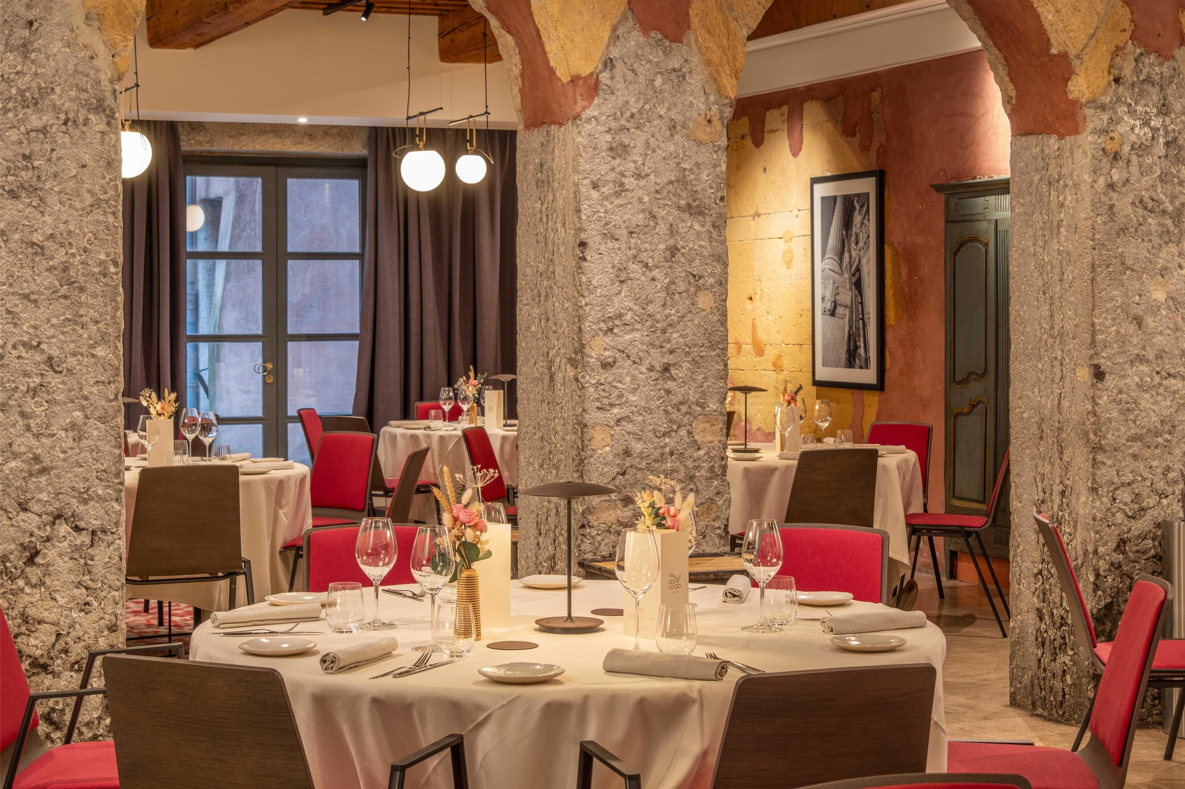 A restaurant with stone walls, red chairs, and tables set for dining.