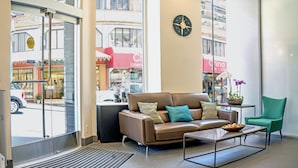 A modern lobby with a leather sofa, a green armchair, a coffee table, and a clock on the wall. - Grant Plaza Hotel (San Francisco)
