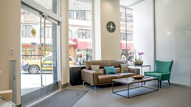 A modern living room with a leather sofa, a coffee table, and a green armchair. A clock is mounted on the wall, and a window offers a view of the street outside. - Grant Plaza Hotel (San Francisco)