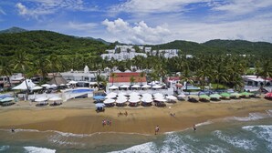 Un complex turístic a la platja amb piscina, parasols i palmeres.