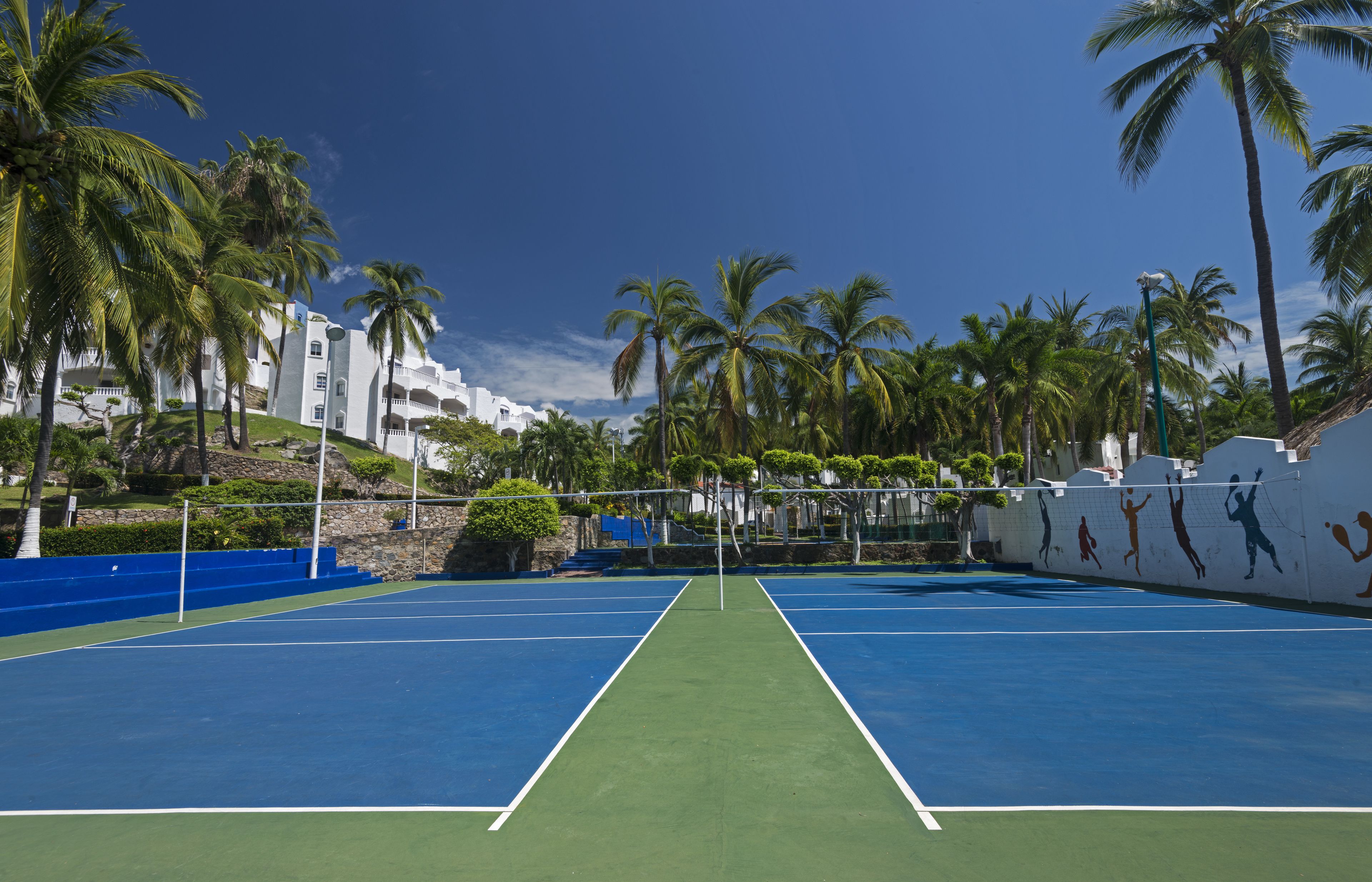 Ein Tennisplatz mit Netz, umgeben von Palmen und weißen Gebäuden.