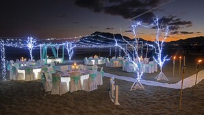 Decoració de boda a l'aire lliure a la platja, amb taules i cadires, llums enfilades i espelmes.