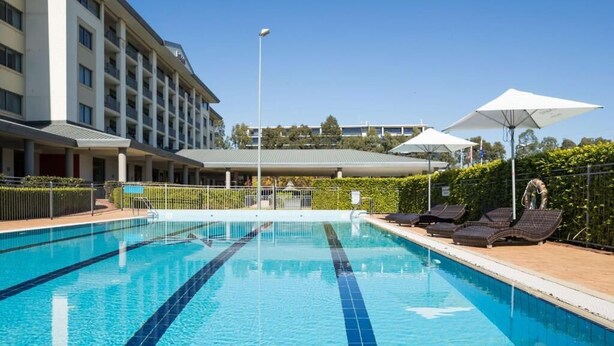 Una piscina con lettini e ombrelloni, circondata da un edificio con diversi piani e balconi.