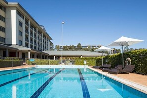 A swimming pool with lounge chairs and umbrellas, surrounded by a building with multiple floors and balconies.