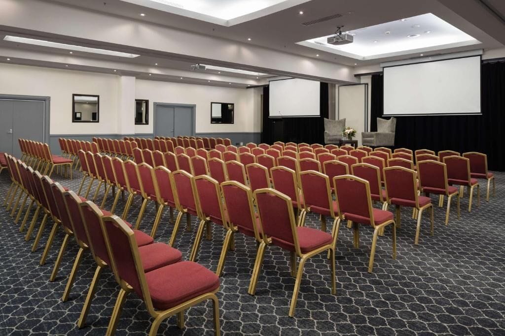 A conference room with rows of red chairs, a projector screen, and a large screen.