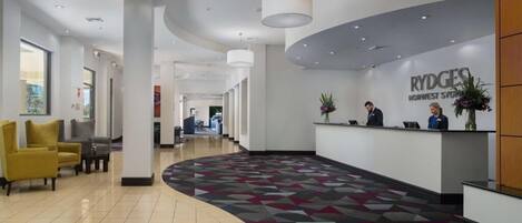 A modern hotel lobby with a reception desk, seating area, and a patterned floor.