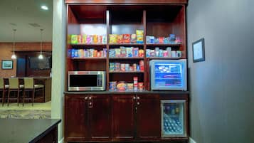 Eine Küchenzeile mit Mikrowelle, Kühlschrank und Vorratsschrank, gefüllt mit Snacks.