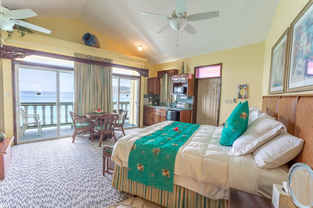 Quarto de hotel com cama, área de refeições, cozinha e varanda com vista para o mar.