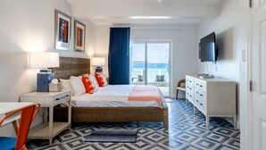 Een slaapkamer met een bed, nachtkastje, lamp, dressoir, televisie en uitzicht op zee.
