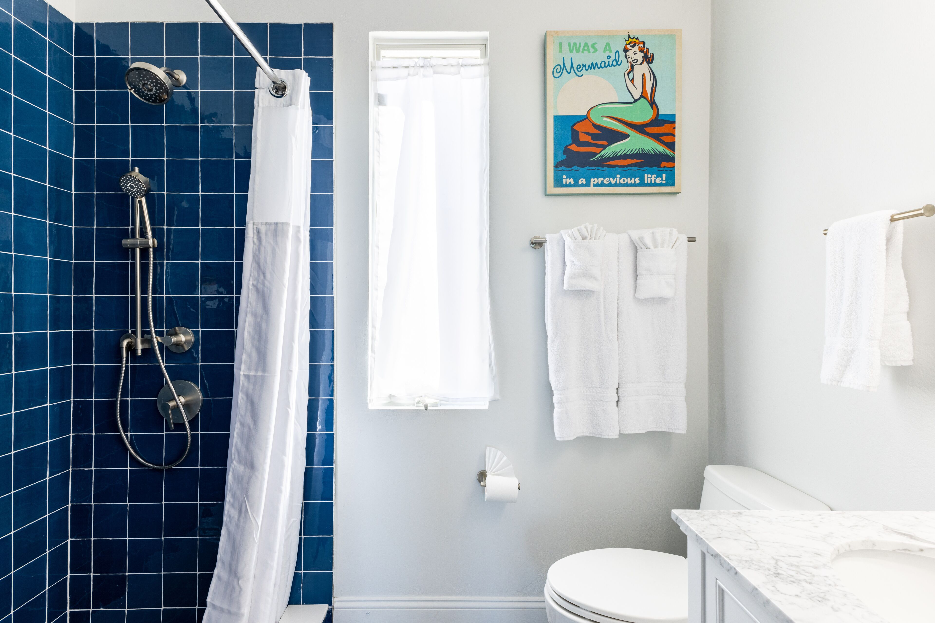 A bathroom with blue tiles, a shower, a toilet, and a marble countertop.