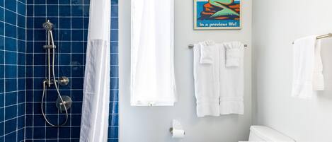 A bathroom with blue tiles, a shower, a toilet, and a marble countertop.