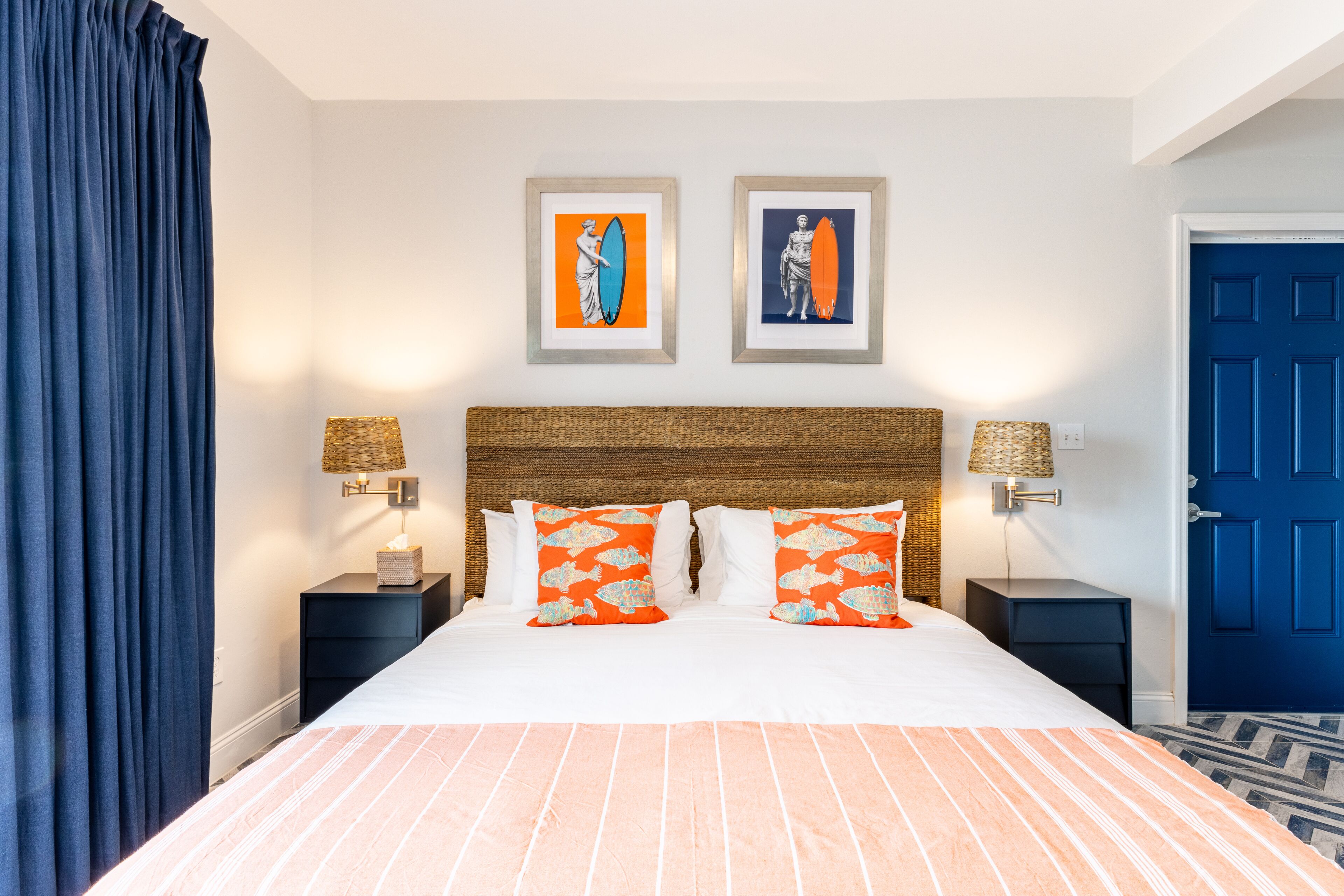 Una habitación de hotel con una cama grande, dos cuadros enmarcados en la pared y una puerta azul.