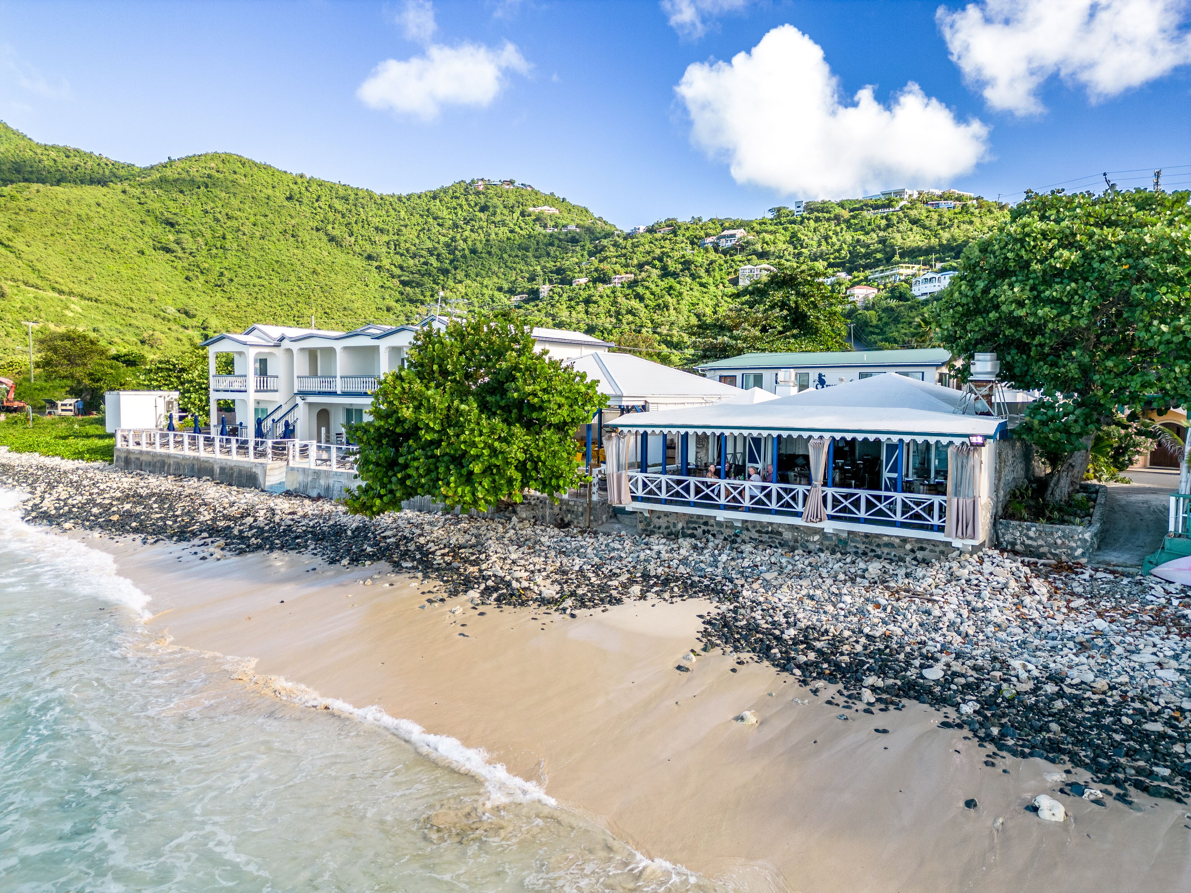 A beachfront property with a large building, a covered patio, and a rocky shoreline.