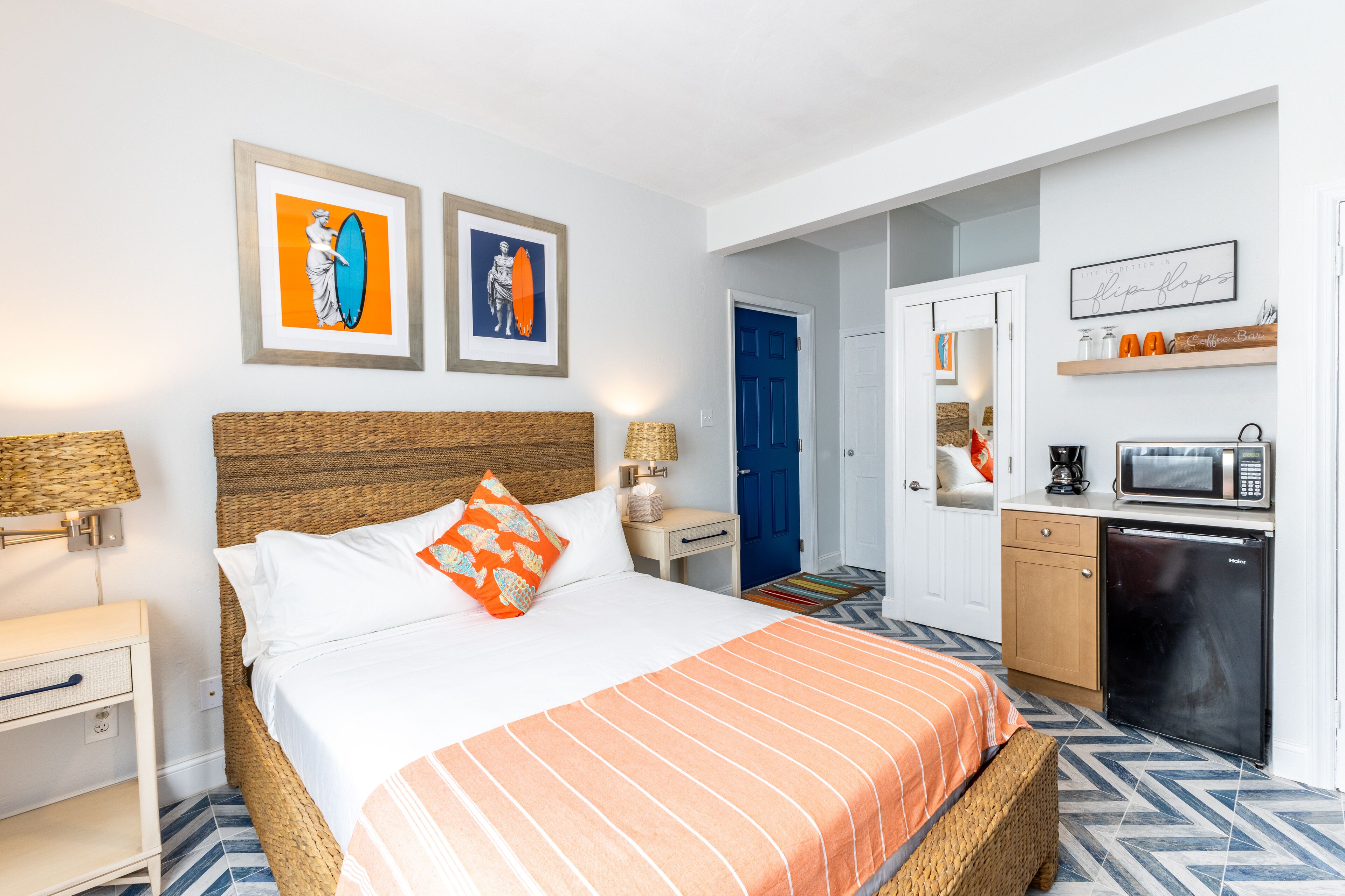 Habitación de hotel con cama, una kitchenette pequeña, baño y puerta que da a otra habitación.