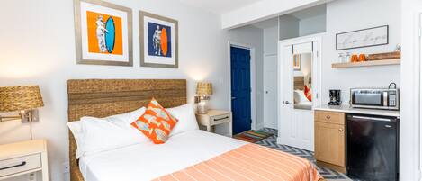 Habitación de hotel con cama, una kitchenette pequeña, baño y puerta que da a otra habitación.