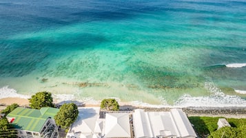 Ett flygbildsbild av ett byggnadskomplex vid kusten, med en strand i förgrunden och havet i bakgrunden.