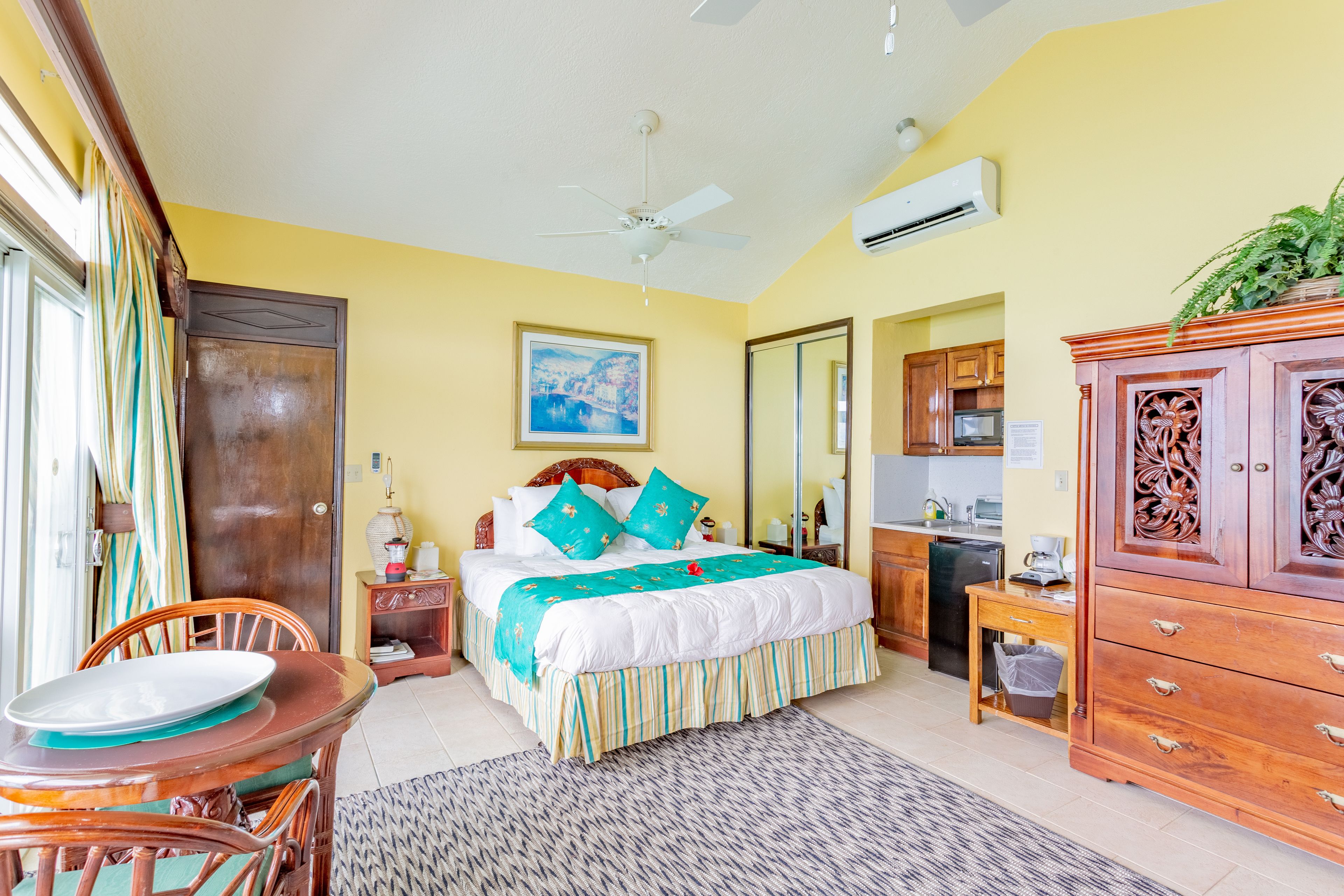 Habitación de hotel con cama, mesa de comedor, aparador de madera y ventilador de techo.