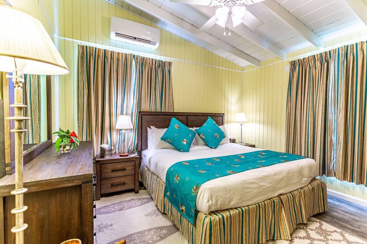 Une chambre d’hôtel avec un lit, des tables de chevet, une lampe, une plante et des rideaux.