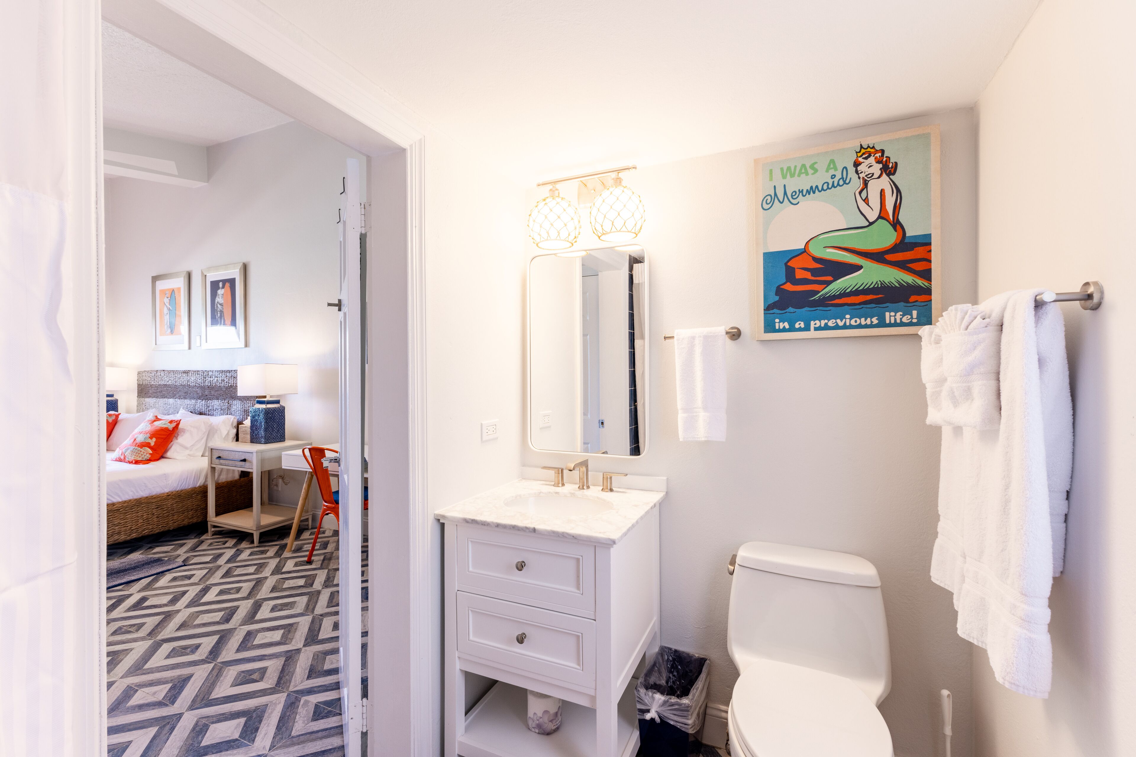 Un baño moderno con lavamanos, espejo y váter blancos. Hay un cartel en la pared y un perchero para toallas.