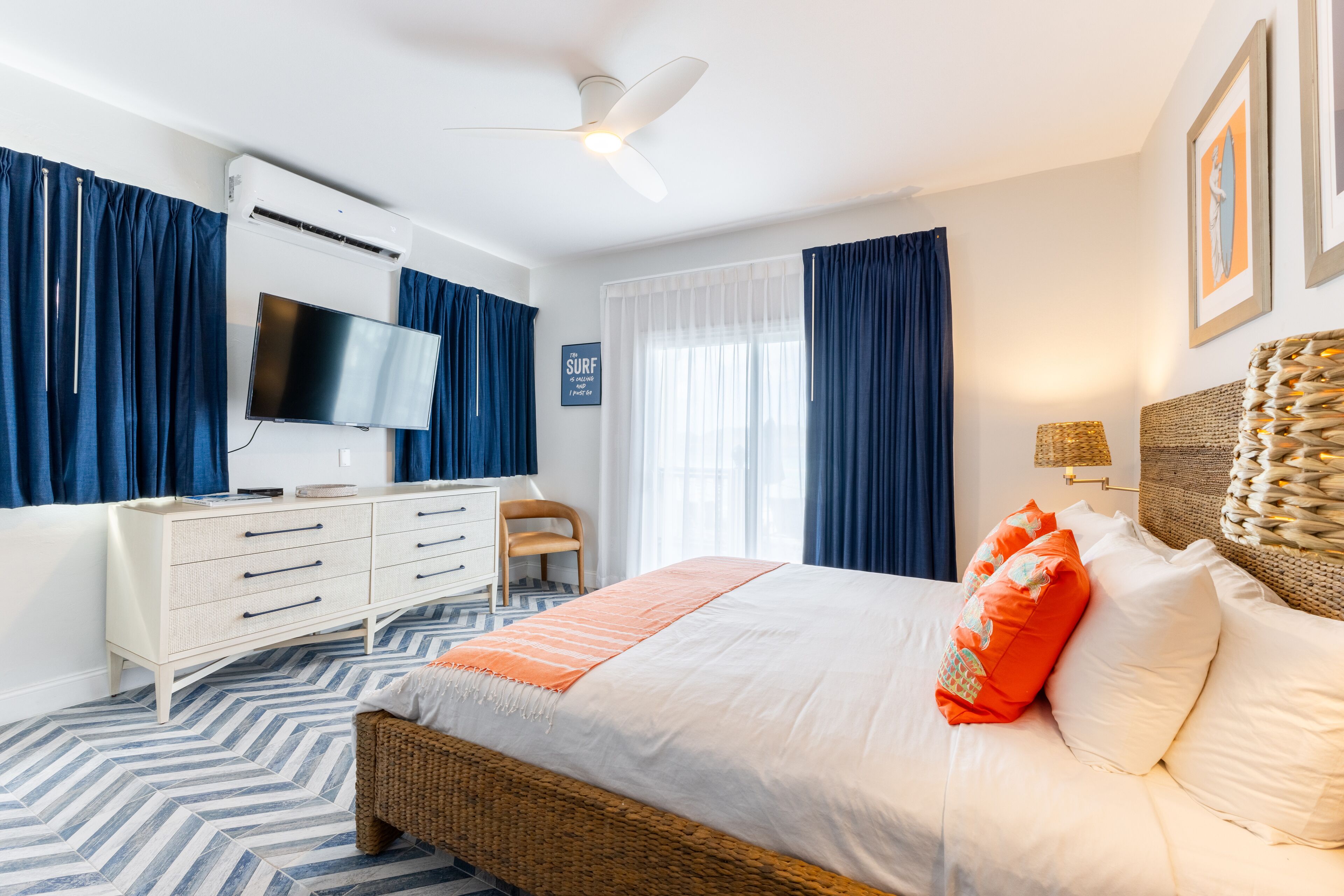 A bedroom with a bed, a television, a dresser, a chair, and a ceiling fan.