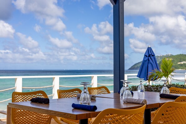 Enjoy meals with a view of the ocean from this dining area, featuring a table set with glassware and comfortable chairs.