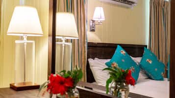 Una habitación de hotel con una cama, dos lámparas de noche, un espejo y un jarrón con flores rojas.