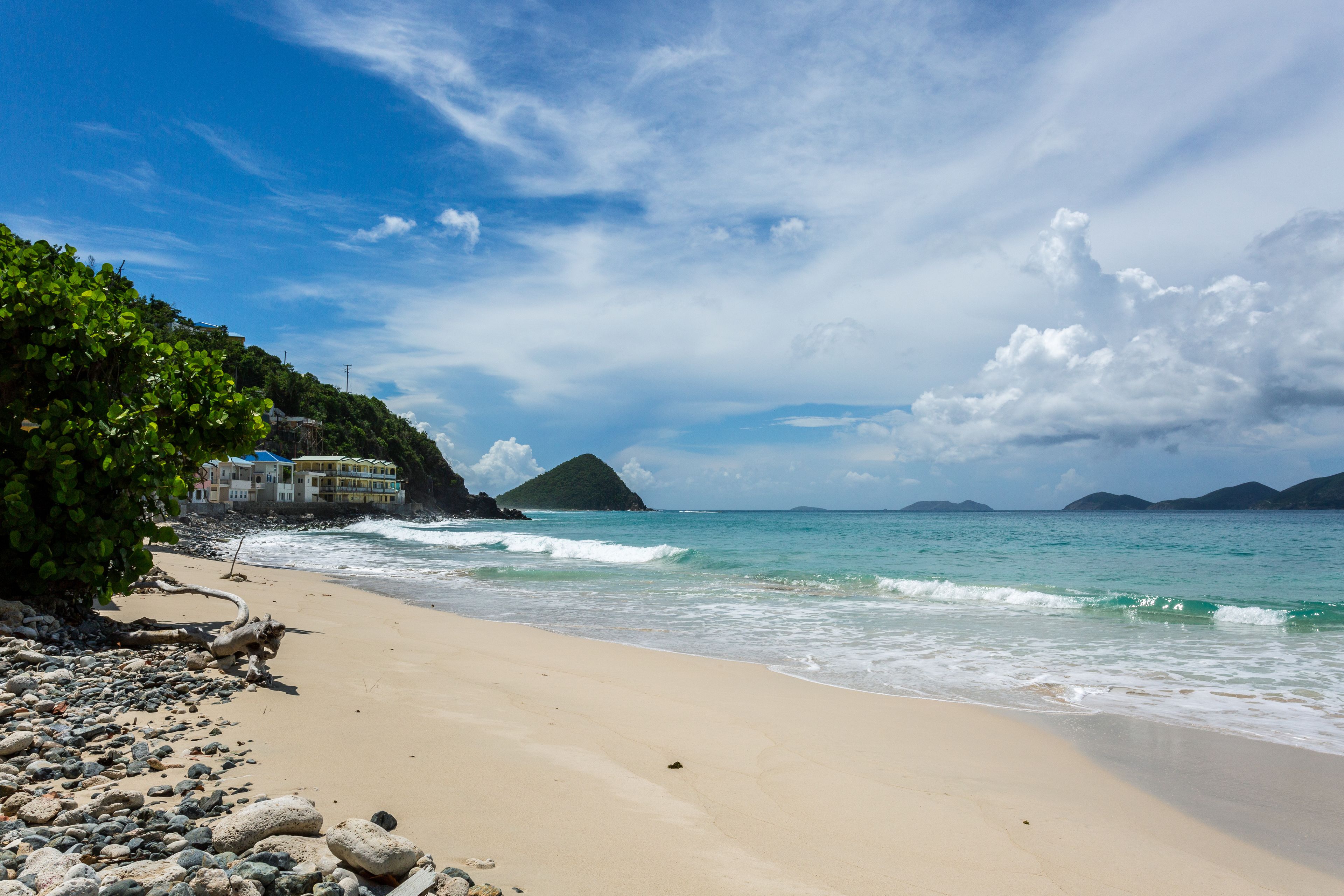 A beach with a rocky shoreline, a building with a yellow roof, and a mountain in the background.
