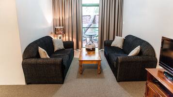 A compact living room with two dark sofas, a wooden coffee table, and a TV stand.