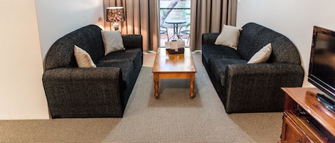 Una sala de estar compacta con dos sofás oscuros, una mesa de centro de madera y un mueble para televisión.